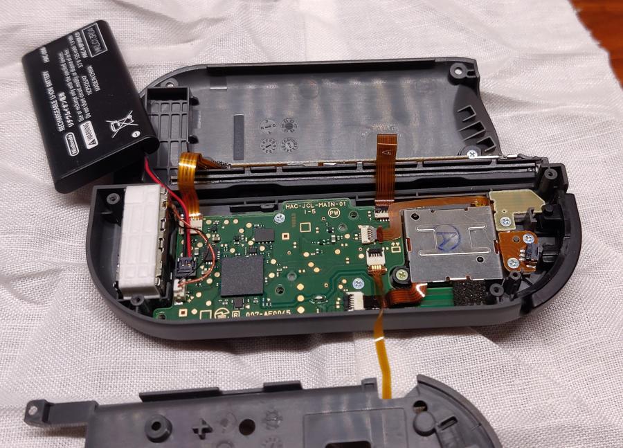 Photograph of a Nintendo Switch Joycon with the case open and the battery out so you can see the circuit boards inside.